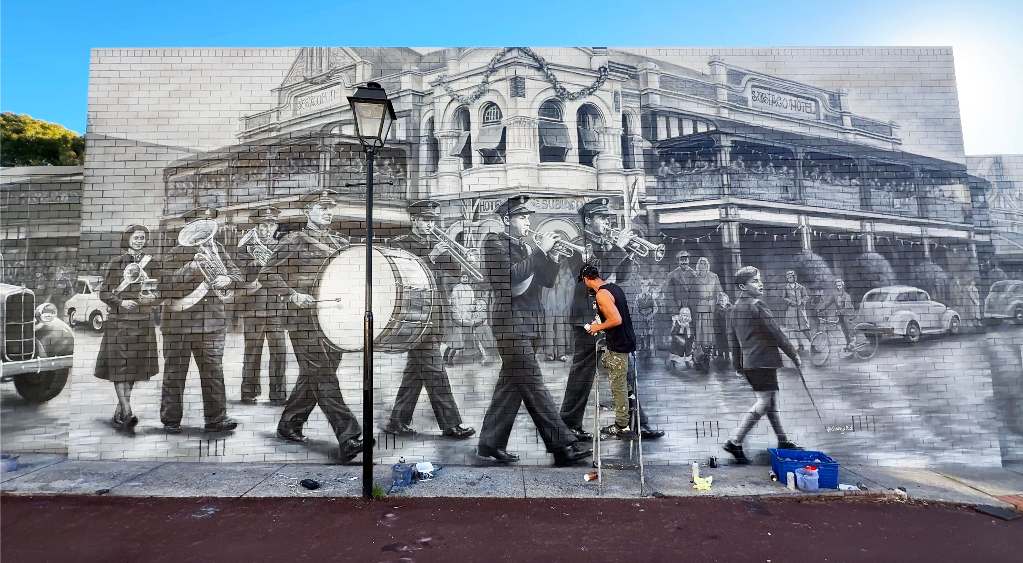 Work underway on the central band and hotel section of the mural, showing the painted figures at building scale.